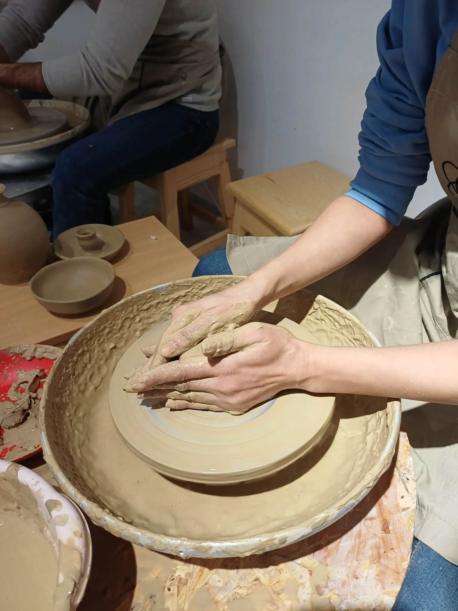 Mains façonnant un grand plat en argile sur un tour de potier